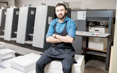 Printer sitting on a stack of papers in front of an offset printing press