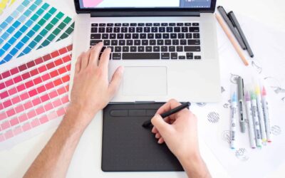 Graphic designer working on a Macbook laptop using a trackpad, color charts and markers