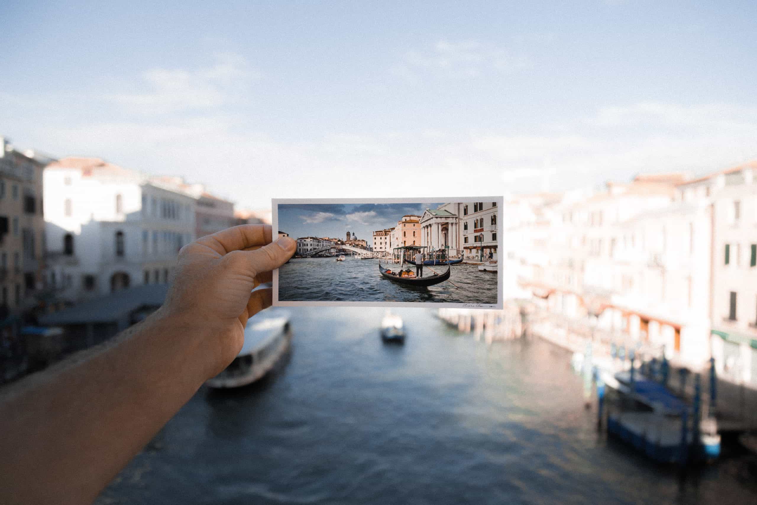 A postcard held up infront of the destination that is pictured on it