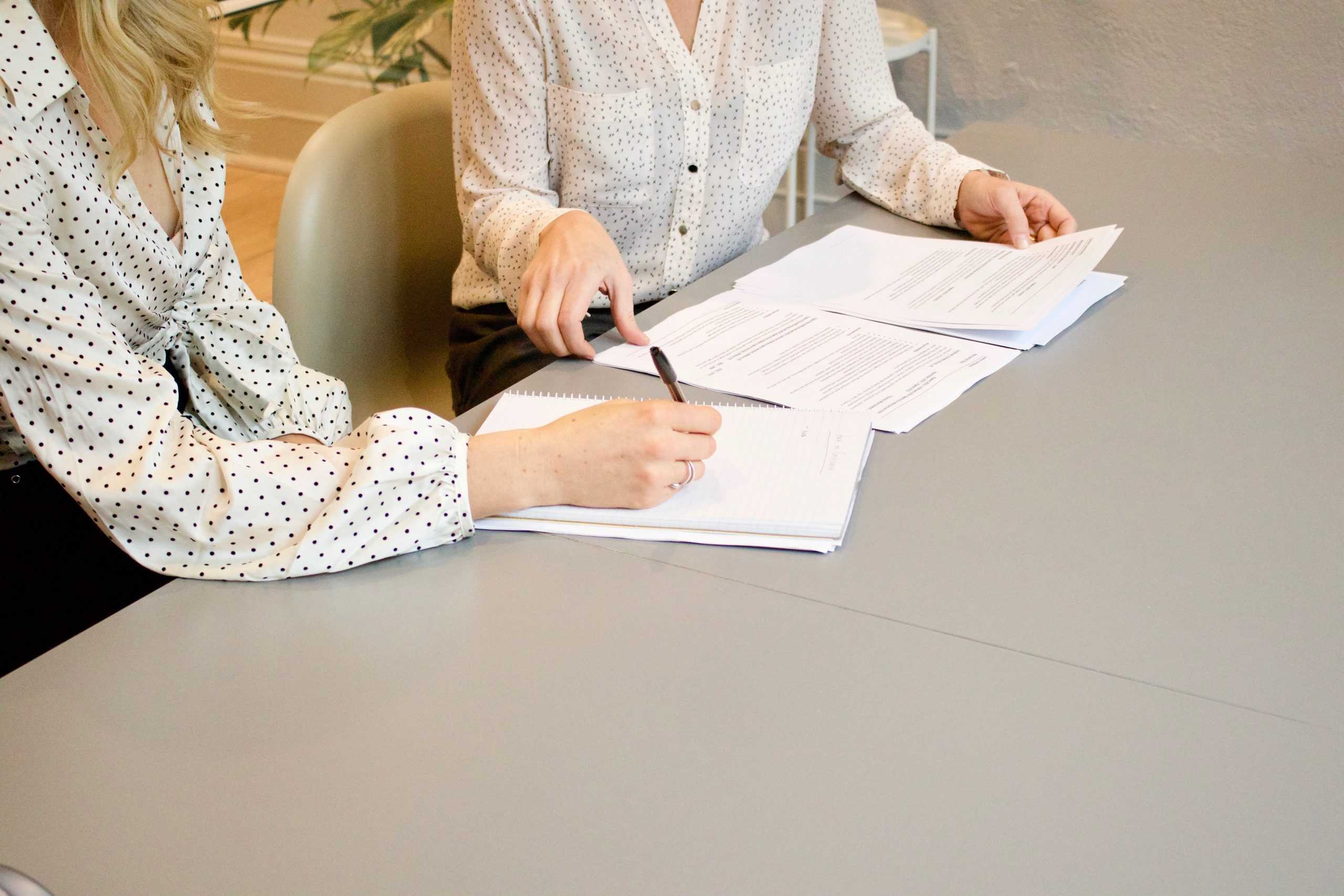 Two women signing papers on a desk