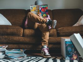 Young man sitting on sofa and reading comics magazine